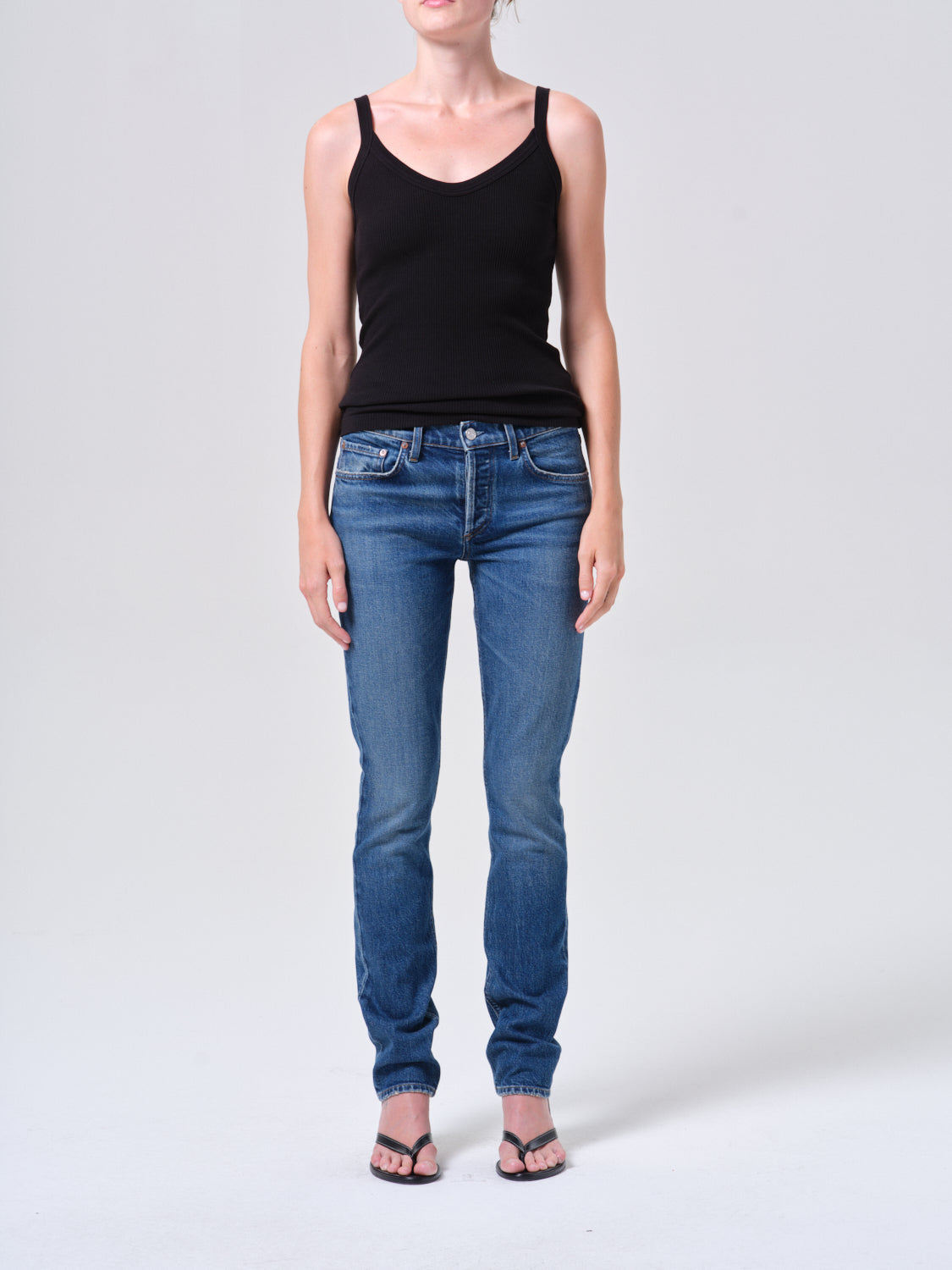 Person wearing a black tank top and blue jeans on a white background