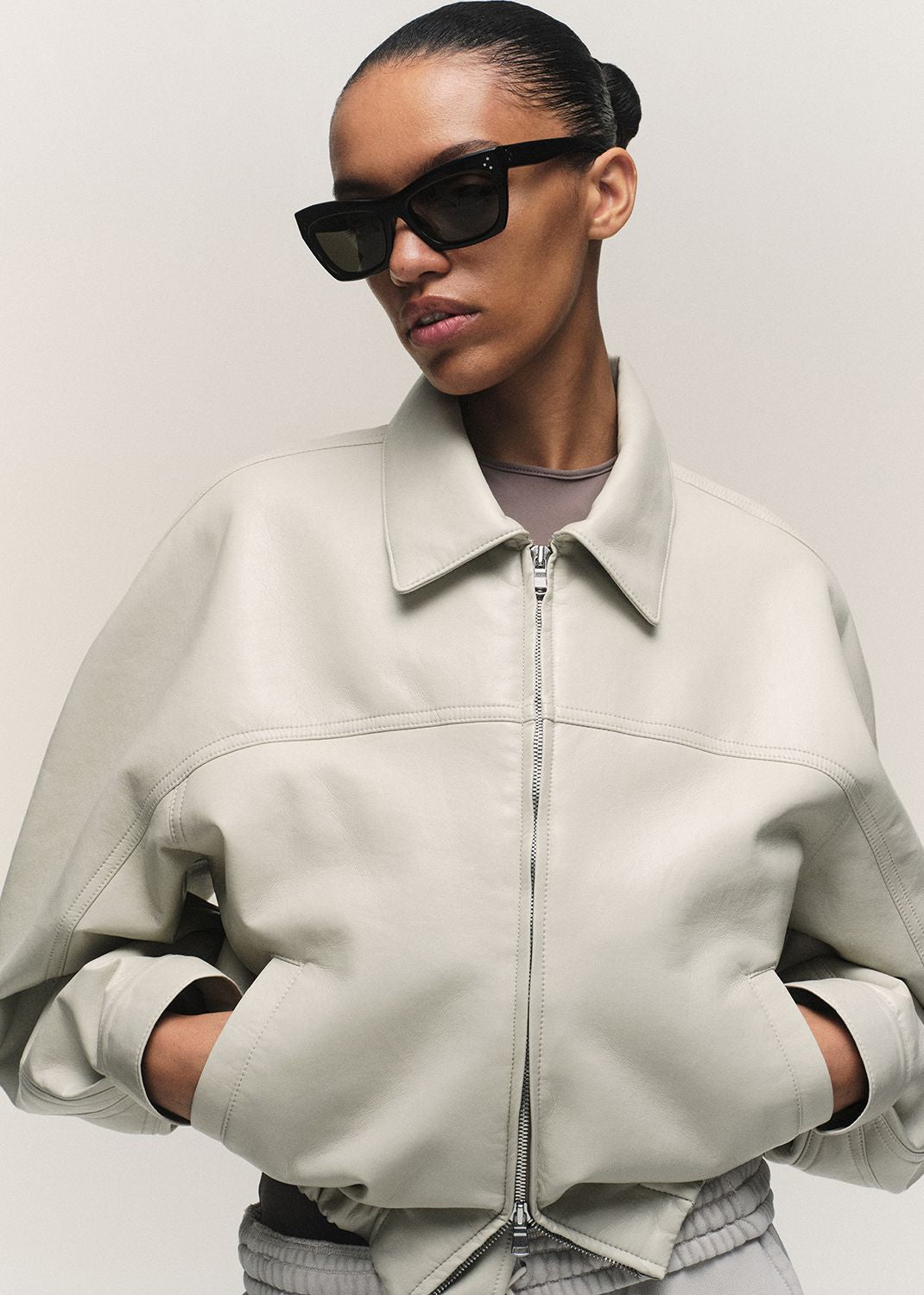 Person wearing a light gray jacket and sunglasses on a plain background