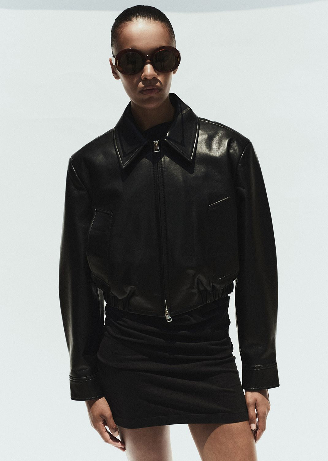 Person wearing a black leather jacket and sunglasses on a white background