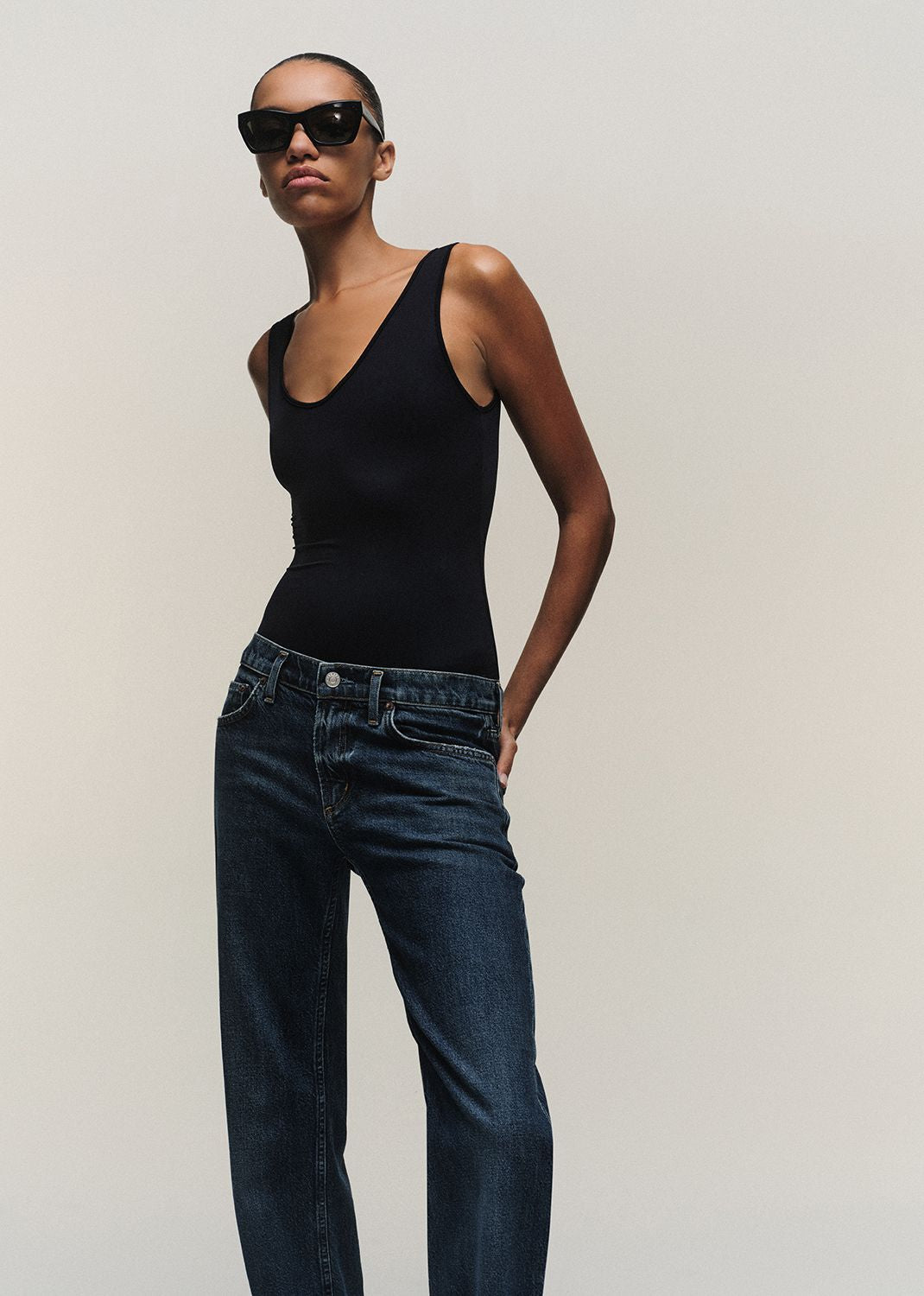 Person wearing a black tank top and blue jeans against a plain background