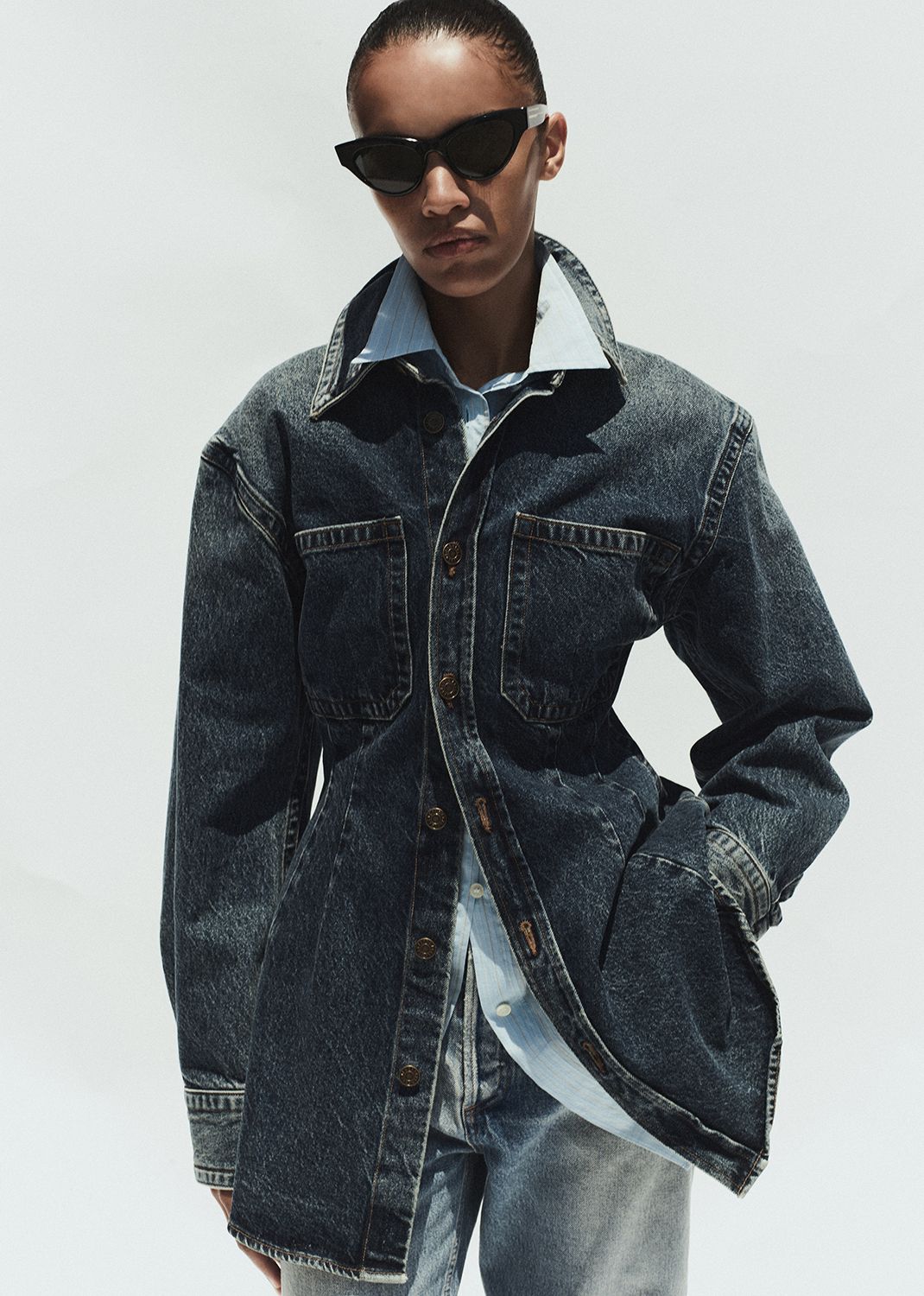 Person wearing a denim jacket and sunglasses on a white background