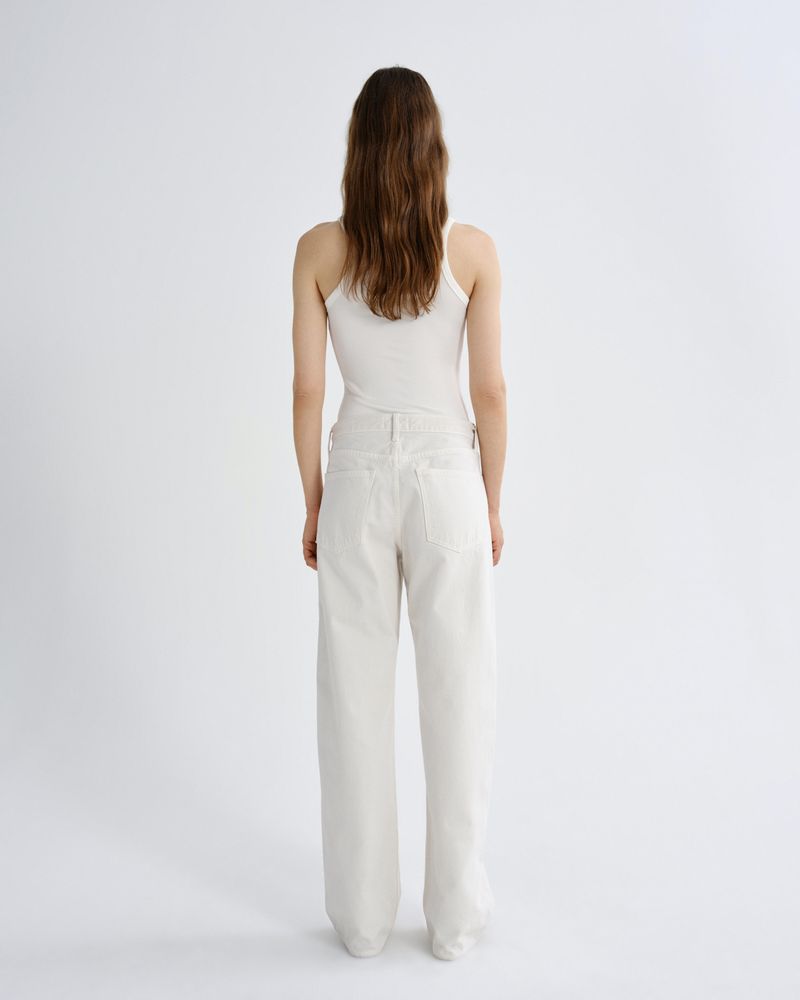 A woman viewed from behind wearing a white ribbed camisole top and high-waisted, wide-leg white trousers against a plain white studio background.