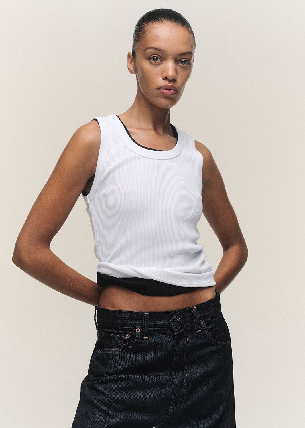 Person wearing a white tank top and black pants against a plain background