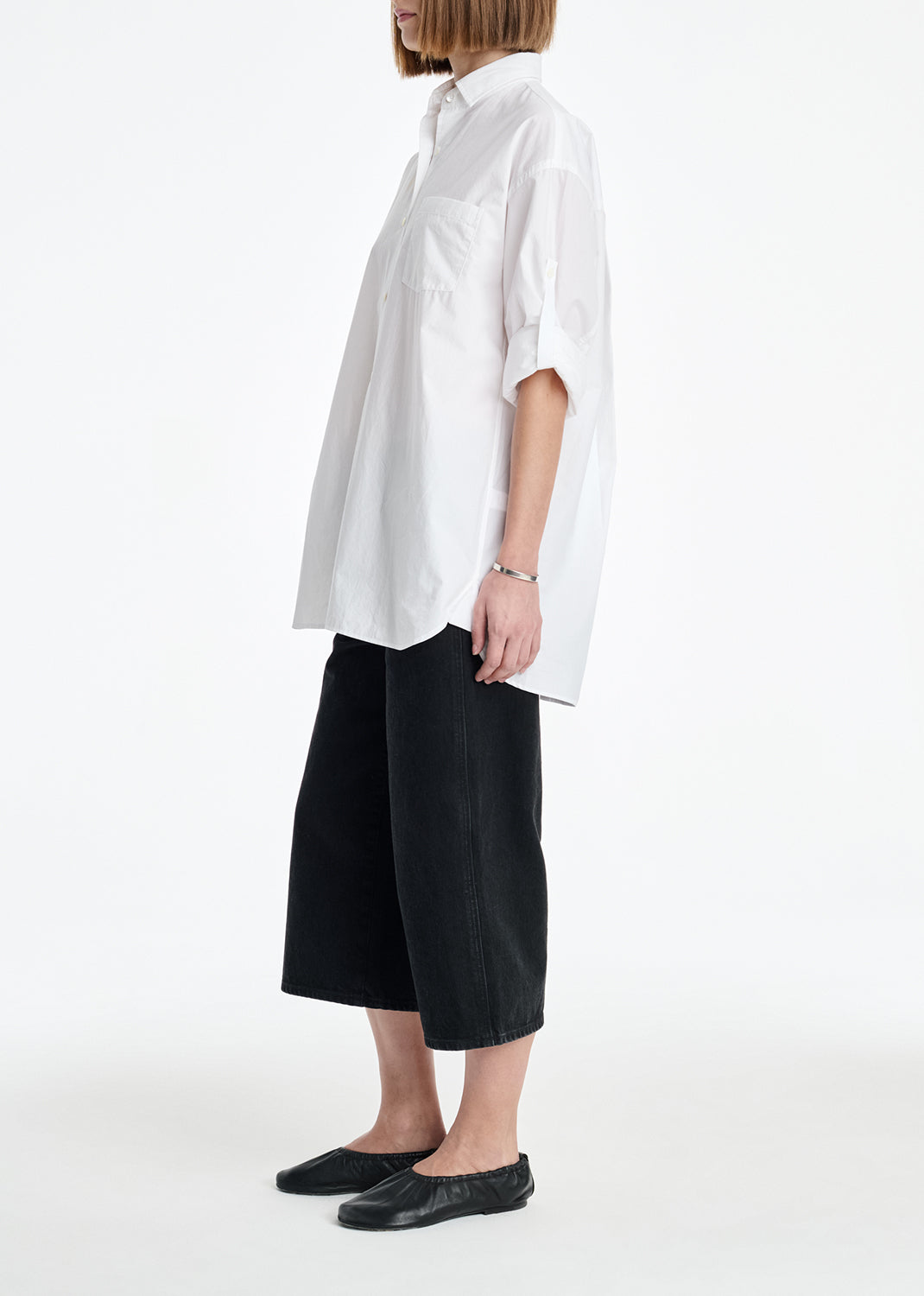 Person wearing a white oversized shirt and black pants on a white background
