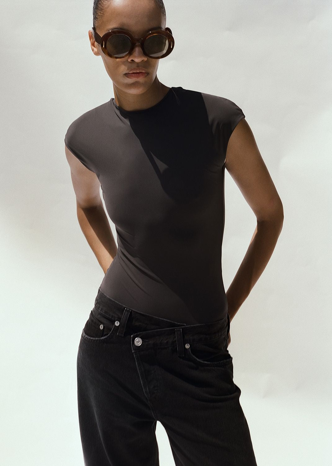 Person wearing a black sleeveless top and black pants with sunglasses on a white background