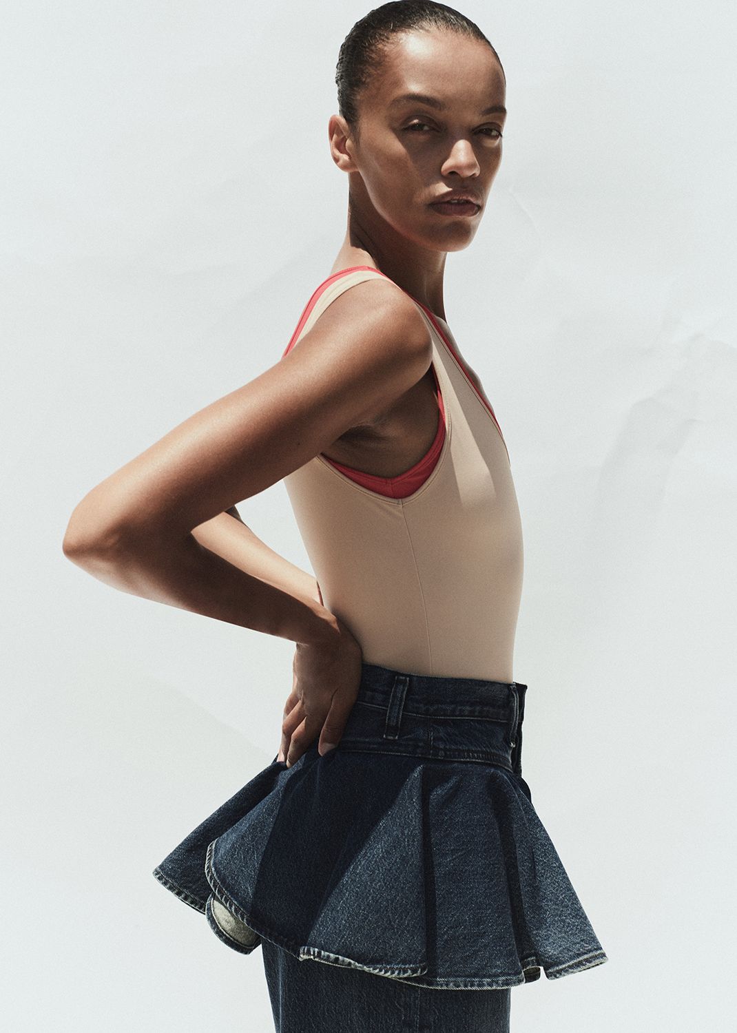 Woman wearing a beige tank top with red straps and a denim skirt on a white background