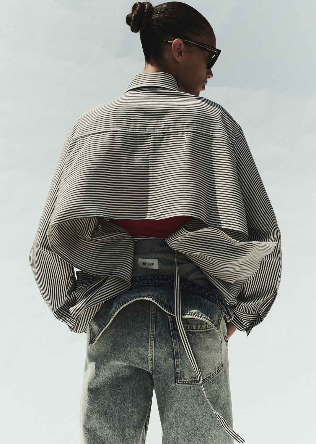 Person wearing a striped shirt and jeans with a plain background